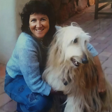 Kate McGahan: Portrait of a woman with her Afghan Hound. A smiling woman lovingly holds a fluffy white Afghan Hound dog.