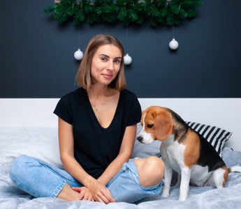 Woman sits on bed with Beagle dog.  Christmas decor in background.