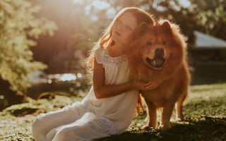 Young girl with long red hair hugs her fluffy Chow Chow dog in a sunny park.