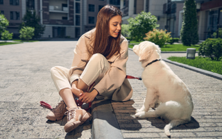Woman sitting on sidewalk, smiling at golden retriever puppy