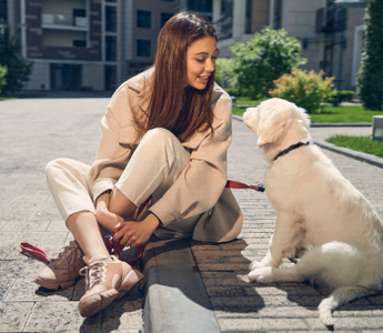 Woman sitting on sidewalk, smiling at golden retriever puppy