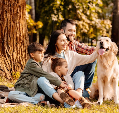 Happy family with kids and Golden Retriever dog enjoying a picnic in the park.