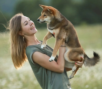 Happy woman holding her Shiba Inu puppy in a field