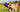 Two Australian Shepherd dogs playing tug-of-war with a blue ball and rope toy in a grassy field.