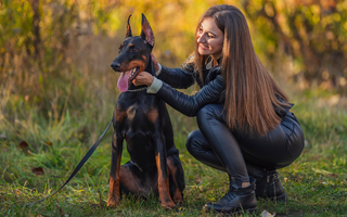 Happy woman petting her Doberman puppy in an autumn park.