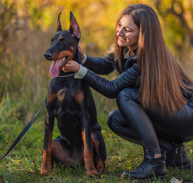 Happy woman petting her Doberman puppy in an autumn park.