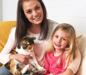 Happy mom and daughter cuddling calico cat on couch