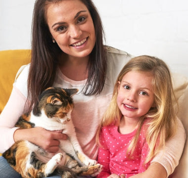 Happy mom and daughter cuddling calico cat on couch