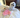 White Maltese dog relaxing on a bed with a pink lamb plush toy.
