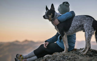 Woman hugs her Australian Cattle Dog at sunset.