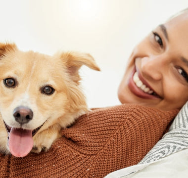 Happy woman cuddling her fluffy golden dog on a couch.