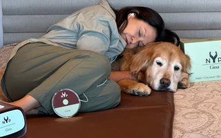 Woman naps with her Golden Retriever, using a Gina device for relaxation.  NYP logo visible.