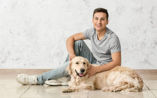 Happy young man sitting on the floor with his Golden Retriever dog.
