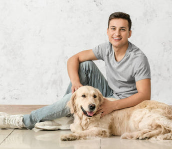 Happy young man sitting on the floor with his Golden Retriever dog.