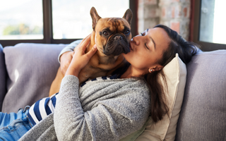 Woman cuddling and kissing her French Bulldog on a couch