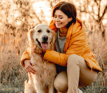 Happy woman cuddling her golden retriever in a field.