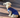 Adorable cream-colored longhaired dachshund puppy wearing a blue sweater sits on a wooden deck.