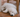 Adorable white puppy sleeping soundly under a wooden chair on a hardwood floor.