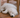 Adorable white puppy sleeping soundly under a wooden chair on a hardwood floor.