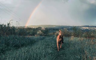 Belgian Malinois dog running in a grassy field with a rainbow in the background.
