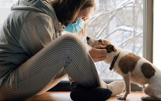 Woman in face mask petting dog by window