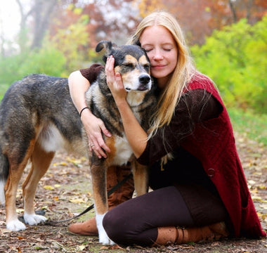 Woman hugs her mixed-breed dog in an autumn forest.