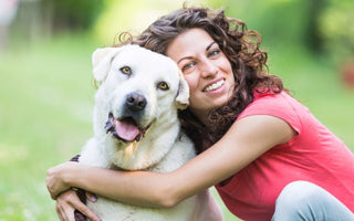 Happy woman hugging her white Labrador Retriever dog outdoors.