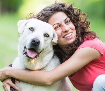 Happy woman hugging her white Labrador Retriever dog outdoors.