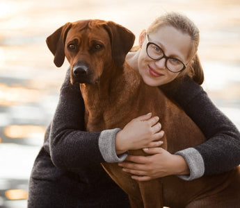 Woman hugging Rhodesian Ridgeback dog near water