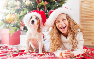 Girl and dog in Santa hats smile for Christmas photo