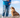 A person in jeans and a blue jacket stands on a rock overlooking a valley, with a brown English Bulldog sitting beside them.