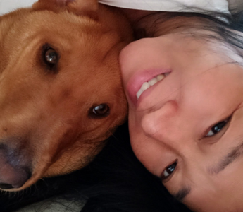 Close-up of a woman and her reddish-brown dog cuddling.