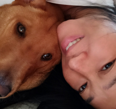 Close-up of a woman and her reddish-brown dog cuddling.