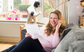Happy woman on sofa reviewing paperwork while talking on phone.