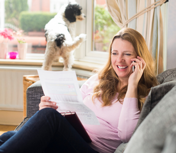 Happy woman on sofa reviewing paperwork while talking on phone.