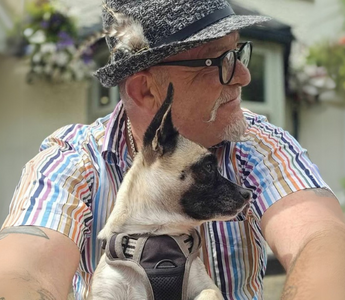 Man in hat and striped shirt cuddling small beige and black dog